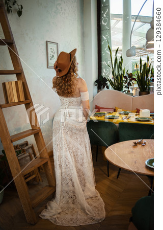 Beautiful slim blonde poses in boho wedding dresses and an embroidered corset on a summer terrace 129384660