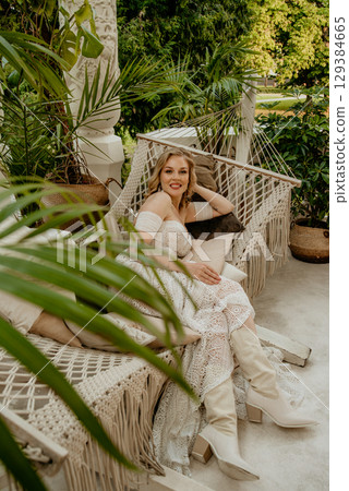 Beautiful slim blonde poses in boho wedding dresses and an embroidered corset on a summer terrace Beautiful slim blonde poses in boho wedding dresses and an embroidered corset on a summer terrace 129384665
