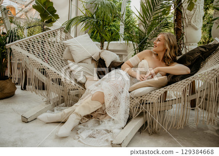 Beautiful slim blonde poses in boho wedding dresses and an embroidered corset on a summer terrace 129384668
