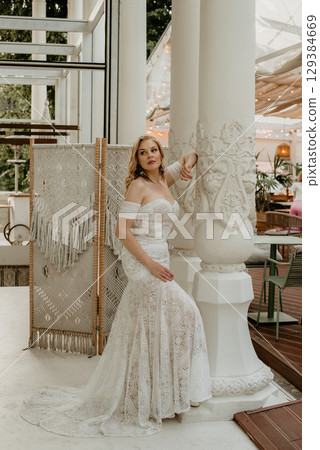 Beautiful slim blonde poses in boho wedding dresses and an embroidered corset on a summer terrace 129384669