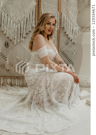Beautiful slim blonde poses in boho wedding dresses and an embroidered corset on a summer terrace Beautiful slim blonde poses in boho wedding dresses and an embroidered corset on a summer terrace 129384671