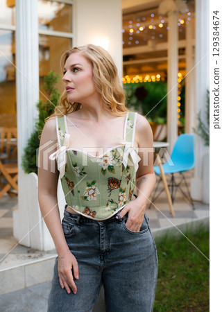 Beautiful slim blonde poses in boho wedding dresses and an embroidered corset on a summer terrace Beautiful slim blonde poses in boho wedding dresses and an embroidered corset on a summer terrace 129384674