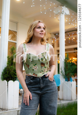 Beautiful slim blonde poses in boho wedding dresses and an embroidered corset on a summer terrace 129384677