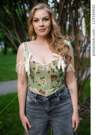 Beautiful slim blonde poses in boho wedding dresses and an embroidered corset on a summer terrace Beautiful slim blonde poses in boho wedding dresses and an embroidered corset on a summer terrace 129384682