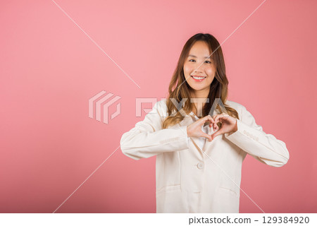 A confident business woman wear suit smiles and creates a heart symbol with two hands on white background. Asian portrait of a beautiful young female expressing love and happiness for Valentine's Day A confident business woman wear suit smiles and creates a heart symbol with two hands on white background. Asian portrait of a beautiful young female expressing love and happiness for Valentine's Day 129384920