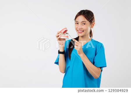 Asian woman, smile, oral model holding dental mirror, showing teeth, in clinic, nurse with dental tool displays the perfect dental care example, headshot isolated studio white background 129384929