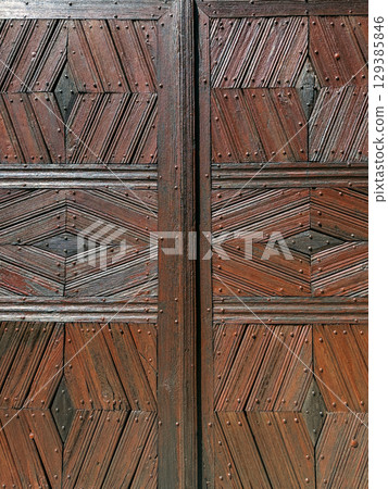 Close-up of a rustic wooden door featuring symmetrical geometric patterns and nail detailing. Traditional craftsmanship, architectural texture, woodworking design, cultural heritage 129385846