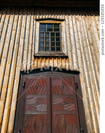 Entrance of a traditional wooden building with a patterned dark wood door and a gridded window above. Architectural heritage, wooden craftsmanship, vernacular design, historical preservation 129385850