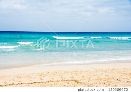 A shallow sandy beach with emerald green waves crashing into it. The coast of Fuerteventura 129386470