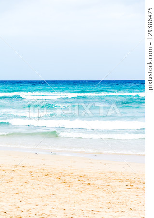 A shallow sandy beach with emerald green waves crashing into it. The coast of Fuerteventura A shallow sandy beach with emerald green waves crashing into it. The coast of Fuerteventura 129386475