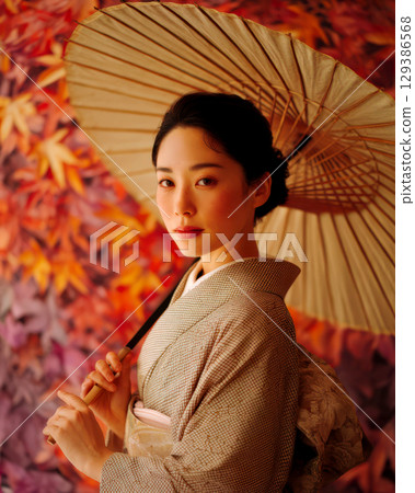 A woman wearing a kimono standing in front of an autumn leaf pattern 129386568