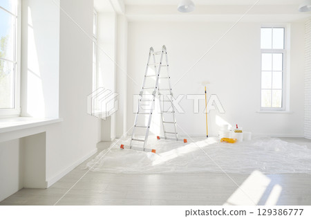 Step ladder, buckets with paint roller standing in empty light room in new house 129386777
