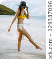 woman in  yellow bikini is walking in the water 129387096