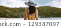 woman wearing  yellow bikini and  black and white hat is standing on  beach 129387097