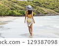 woman is walking on the beach wearing  yellow bikini and  white hat 129387098