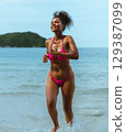 woman in  pink bikini is running in the ocean 129387099