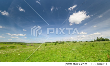 A Vibrant Green Field Lushly Spreads Under a Bright Blue Sky with Beautiful Fluffy Clouds 129388051