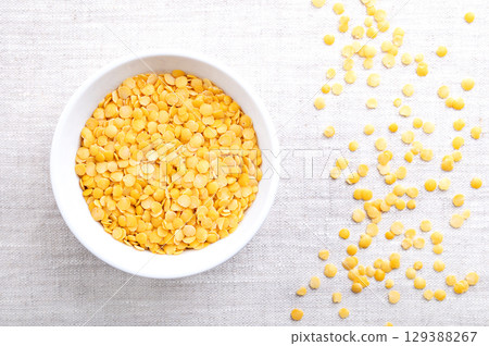 Yellow lentils, in a white bowl, on linen. Dried seeds of a Lens esculenta variety, a legume of small, round, and yellow fruits. High in protein and fiber, with soft and creamy texture, when cooked. Yellow lentils, in a white bowl, on linen. Dried seeds of a Lens esculenta variety, a legume of small, round, and yellow fruits. High in protein and fiber, with soft and creamy texture, when cooked. 129388267