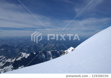 Tranquil Lake With Lush Green Forest, Snow-Capped Mountain, Blue Sky And White Clouds 129388330