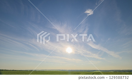 A serene sky with warm sunlight and fluffy clouds stretches over a vibrant green field A serene sky with warm sunlight and fluffy clouds stretches over a vibrant green field 129388732