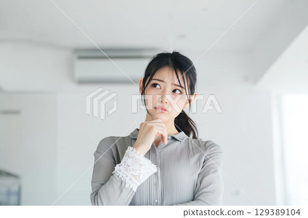 The expression of a young woman who is worried about whether to repair or replace her broken air conditioner 129389104
