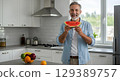 happy senior man eating watermelon in the kitchen 129389757