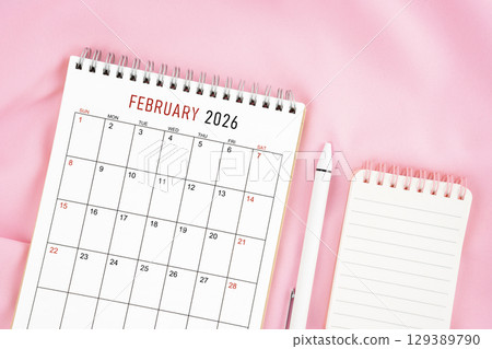 February 2026 month calendar and pen with open diary on pink color fabric background. 129389790