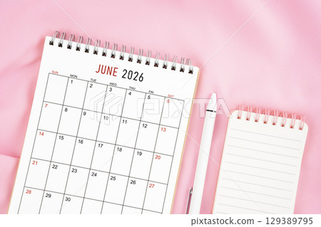 June 2026 month calendar and pen with open diary on pink color fabric background. 129389795