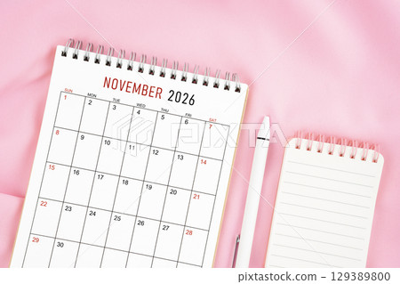 November 2026 month calendar and pen with open diary on pink color fabric background 129389800