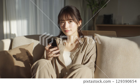 Young woman sitting on sofa and looking at smartphone Young woman sitting on sofa and looking at smartphone 129390654