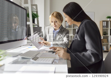 Two female financial accountants reviewing financial documents and analyzing spreadsheet in office. 129390924