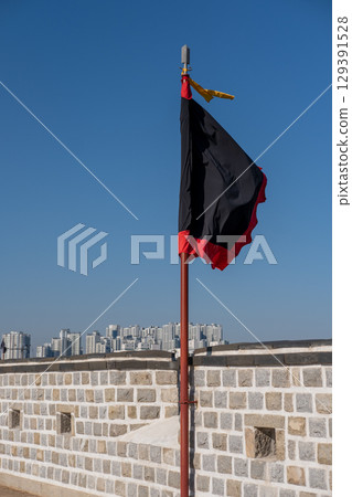 Black and red flag, at Suwon Hwaseong Fortress Wall, with the building view on the background. The wall is surrounding the center of Suwon, the provincial capital of Gyeonggi-do, in South Korea Black and red flag, at Suwon Hwaseong Fortress Wall, with the building view on the background. The wall is surrounding the center of Suwon, the provincial capital of Gyeonggi-do, in South Korea 129391528