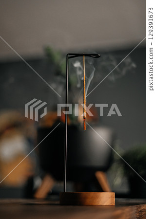 Incense stick smoldering in holder, burning candles, dry flowers and Tibetan singing bowl on wooden table outdoors 129391673