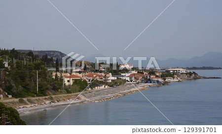 Charming coastal village in Greece showcasing serene waterfront homes, rocky beach, and peaceful blue waters under bright sunshine, perfect for relaxation and exploration 129391701