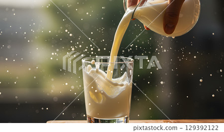 Milk pouring into glass with splash and droplets in natural light, fresh and creamy 129392122