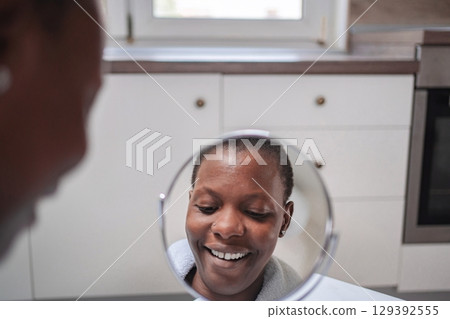 Young woman looking at herself smiling in the mirror in the bathroom 129392555