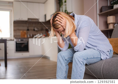 Sad woman sitting on sofa holding head in hands at home Sad woman sitting on sofa holding head in hands at home 129392581