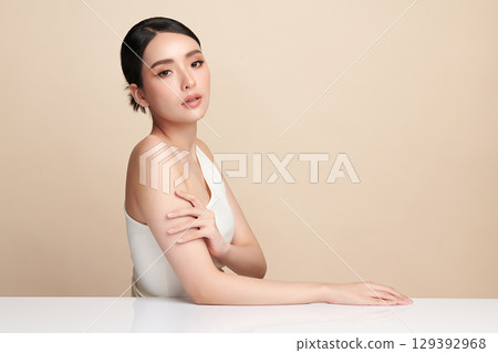 A beautiful young Asian woman with clean, fresh skin against a beige background. Skincare, facial treatment, cosmetology, beauty, and spa. An elegant portrait of an Asian woman. A beautiful young Asian woman with clean, fresh skin against a beige background. Skincare, facial treatment, cosmetology, beauty, and spa. An elegant portrait of an Asian woman. 129392968