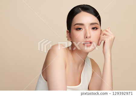 A beautiful young Asian woman with clean, fresh skin against a beige background. Skincare, facial treatment, cosmetology, beauty, and spa. An elegant portrait of an Asian woman. A beautiful young Asian woman with clean, fresh skin against a beige background. Skincare, facial treatment, cosmetology, beauty, and spa. An elegant portrait of an Asian woman. 129392971