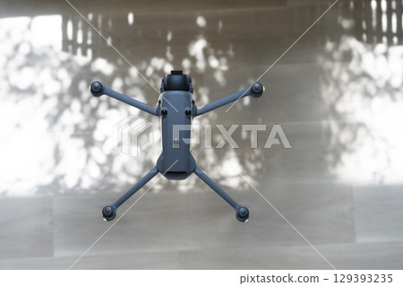 Drone equipped with camera on a wooden surface showcasing intricate shadows from nearby foliage Drone equipped with camera on a wooden surface showcasing intricate shadows from nearby foliage 129393235