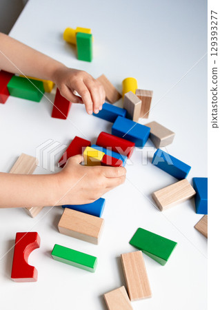 Child playing with colorful wooden building blocks on white surface 129393277