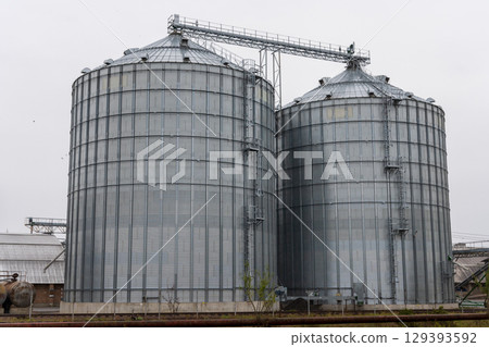 Metal silos stand prominently at an agricultural site, designed for efficient grain storage under cloudy skies 129393592