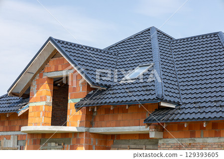 New residential building features a black tiled roof with brick walls nearing completion against a clear blue sky New residential building features a black tiled roof with brick walls nearing completion against a clear blue sky 129393605