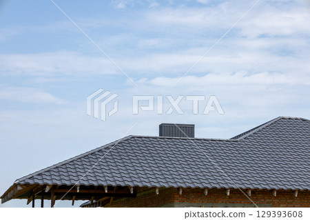 Construction of a new house showcases a gray tiled roof under a clear blue sky, reflecting progress in suburban development Construction of a new house showcases a gray tiled roof under a clear blue sky, reflecting progress in suburban development 129393608