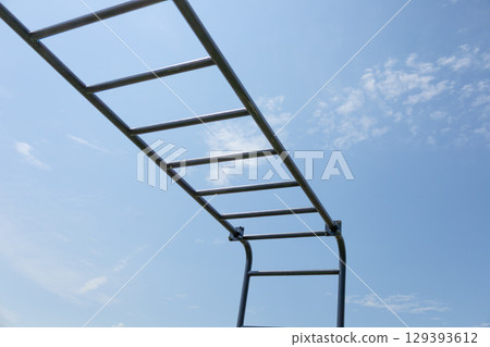 Children play on a monkey bar structure, enjoying a sunny afternoon under a bright blue sky and fluffy clouds Children play on a monkey bar structure, enjoying a sunny afternoon under a bright blue sky and fluffy clouds 129393612