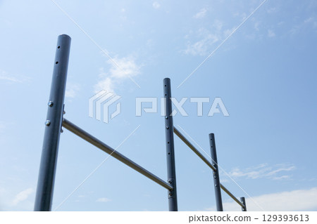 Vertical bars create a workout station for users in a serene park setting under a bright sky with few clouds 129393613