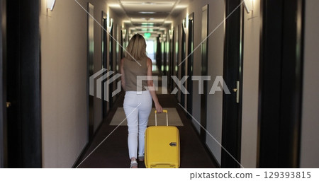 Woman walk at hotel corridor with suitcase. Rear view. Representing business or leisure travel experience. Woman walk at hotel corridor with suitcase. Rear view. Representing business or leisure travel experience. 129393815