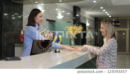 Woman check in at reception, entering hotel and gets key card at front desk. Hotel concierge worker welcoming tourist at resort. 129393857