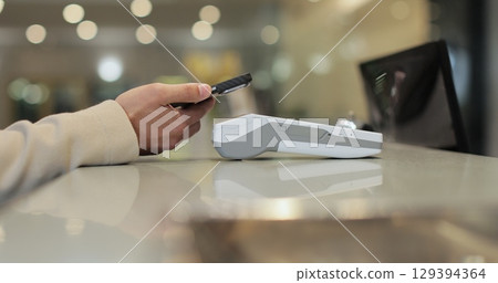 Customer with mobile phone pay for hotel reception, payment. Client, concierge service or people at help desk. Person at reception desk and doing check. Close up. Customer with mobile phone pay for hotel reception, payment. Client, concierge service or people at help desk. Person at reception desk and doing check. Close up. 129394364