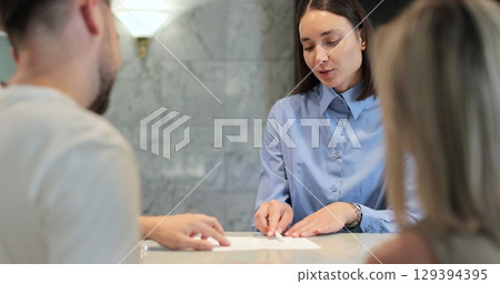Man and woman walks up to desk and signs papers, takes keys and talks to female. Man signs papers, takes keys and talks to female manager. Man and woman walks up to desk and signs papers, takes keys and talks to female. Man signs papers, takes keys and talks to female manager. 129394395